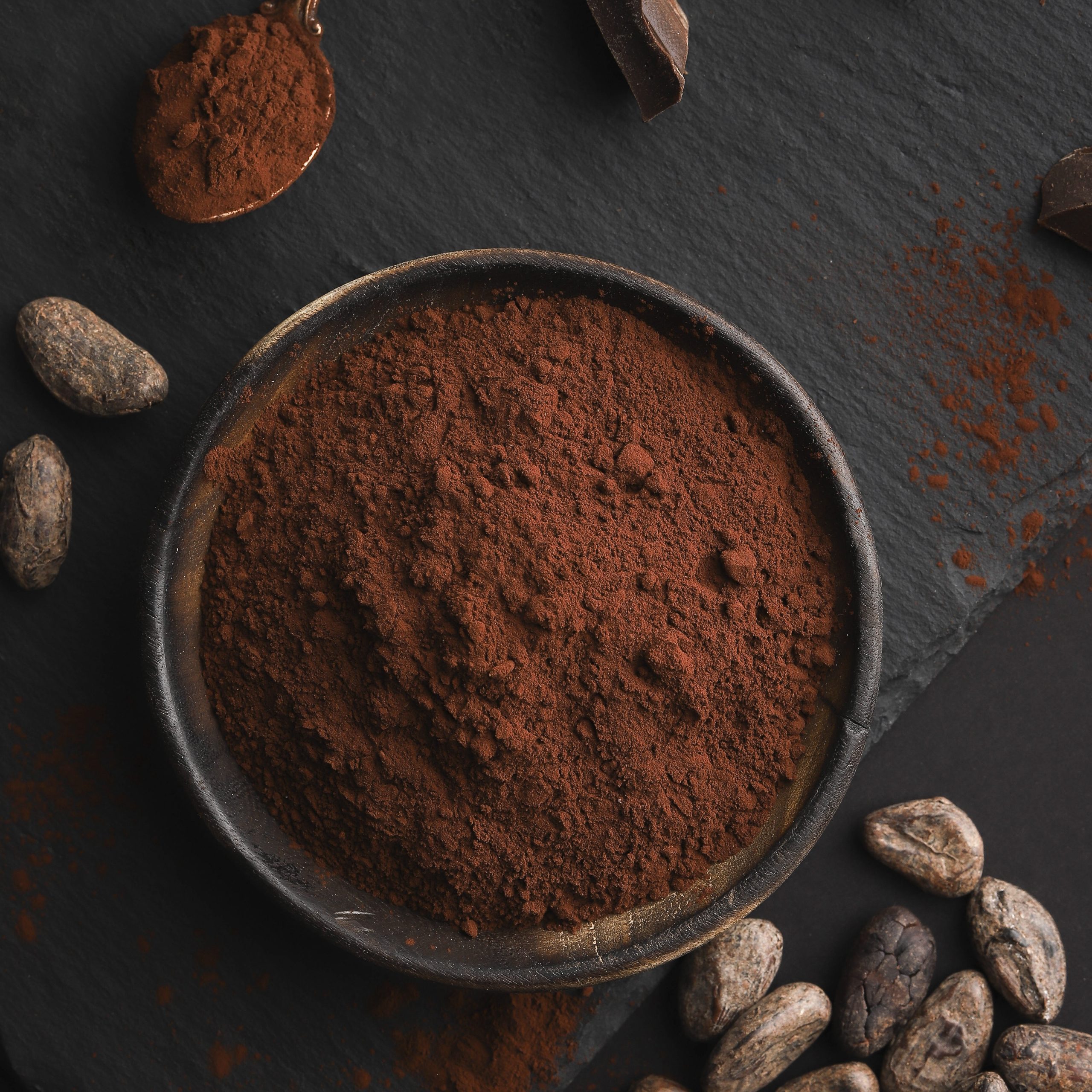 Broken chocolate nuts pieces, cocoa bens and cocoa powder on dark stone background.